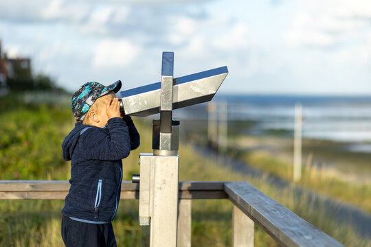 Child observes scenic landscape through binoculars on a beach boardwalk during the day