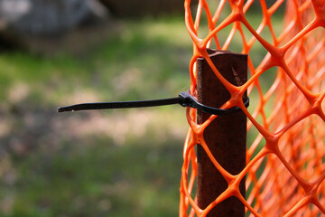 close-up of an orange safety fence with a cable tie used as a barrier around landscaping. this roll...