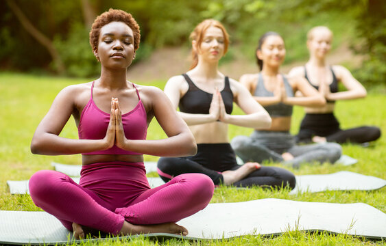 Yoga for inner peace. Diverse young women meditating in lotus pose and doing namaste gesture at park
