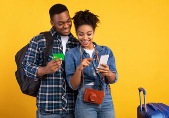 Happy Black Couple Booking Travel Tickets Online Using Smartphone And Credit Card Standing With...