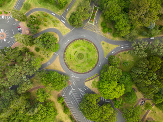 People and cars move through a large roundabout and parking area within a green park, captured from...