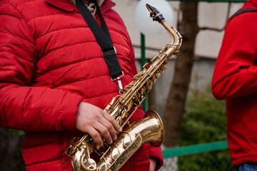 Naklejka premium Saxophone Player in Red Puffer Jacket Performing Outdoors. Brass Instrument, Street Musician, Golden Sax, Music, Urban Scene, Winter Clothing