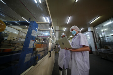 Workers examine machinery in a production facility while discussing operations and safety