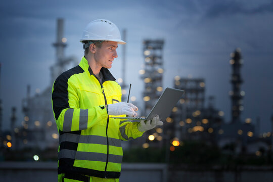 Industrial worker using laptop at night in a refinery environment