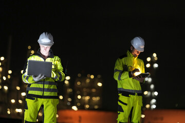 Construction workers analyze data at night in a busy industrial area