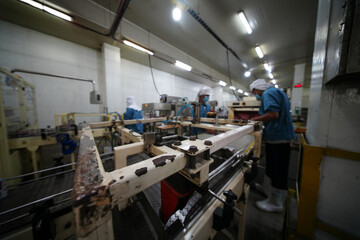 Workers operate machinery in a manufacturing facility during daytime production hours