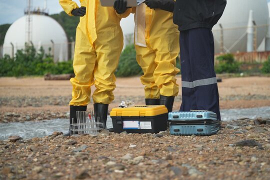 Workers in protective gear conduct environmental testing at oil facility site during daylight