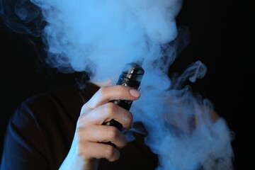 Woman using electronic smoking device in neon lights on black background