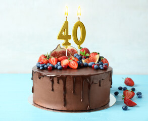 Yummy chocolate cake with fruits and burning number shaped candles on light blue table. 40th...