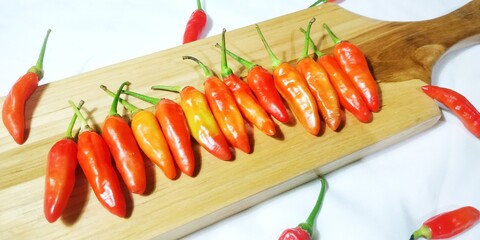 Horizontal Line of Fresh, Uncooked Chili Peppers in Warm Red and Orange Hues, Presented on a Wooden...