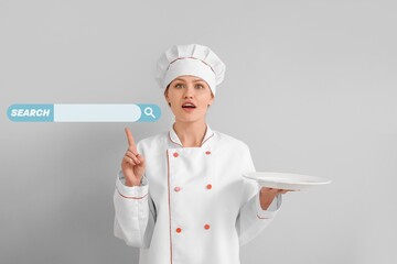 Female chef pointing at web search engine against grey background