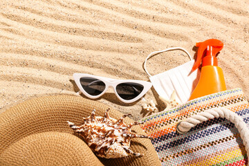 Bag with bottle of sunscreen cream, medical mask, beach accessories and seashells on sand. Melanoma...