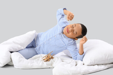 Little African-American boy with soft blanket lying on light background