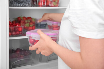 Woman taking cherry in plastic container from refrigerator, closeup