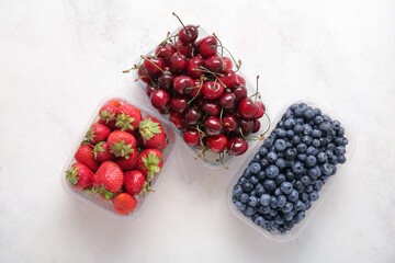 Plastic containers with fresh blueberry, cherry and strawberry on light background