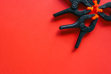 Four black plastic spring clamps with orange tips arranged diagonally on bright red background. Minimalistic tool concept with strong contrast and copy space