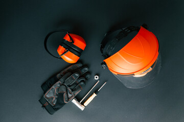 Safety face shield, earmuffs, work gloves, screwdriver, wrench and nut arranged on dark background....