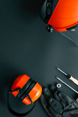 Flat lay of brush cutter head, protective helmet with face shield, ear muffs, gloves, screwdriver, wrench and nut on black background, complete gardening and landscaping safety set