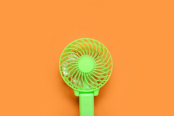 Portable green electric fan on orange background, closeup
