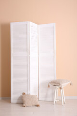 Folding screen, stool and pillows near beige wall