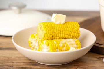 Bowl of boiled corn cobs with butter on wooden table in kitchen