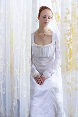 A Regency period woman wearing a white embroidered cotton dress and surrounded by backlit lace...
