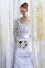 A Regency period woman wearing a white embroidered cotton dress and surrounded by backlit lace...