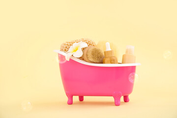 Small bathtub with different bath supplies on color background
