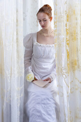 A Regency period woman wearing a white embroidered cotton dress and surrounded by backlit lace...