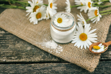 Natural skincare setup with amber cosmetic bottles, a small jar of white cream, chamomile flowers,...