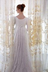 A Regency period woman wearing a white embroidered cotton dress and surrounded by backlit lace...