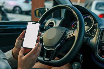 Person holding smartphone with blank screen behind steering wheel inside modern car. Navigation or...