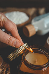 A hand lighting a candle in a cozy baking setup with cinnamon buns, flour, sugar, and eggs on a dark surface, ideal for warm kitchen scenes