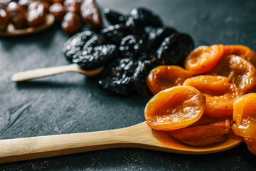 Four types of dried fruits-cranberries, dates, prunes, and apricots-arranged in rows on a dark...