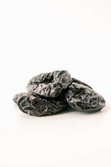 Close-up of glossy dried prunes stacked on a clean white background, showcasing their wrinkled...