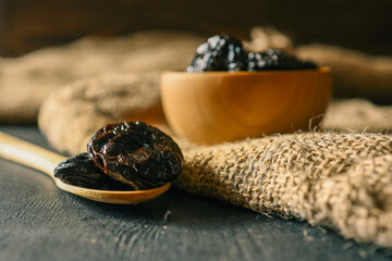 Wooden bowl filled with dried prunes on rustic burlap and wooden background. Natural, healthy snack...