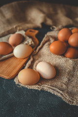 Fresh farm eggs in various shades of brown and cream on burlap and wooden boards. Rustic kitchen setting with wooden spoons, jute twine, and natural light