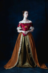 A red-haired Renaissance woman wearing an embroidered silk ensemble against a studio backdrop