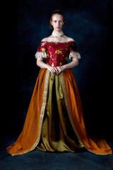 A red-haired Renaissance woman wearing an embroidered silk ensemble against a studio backdrop