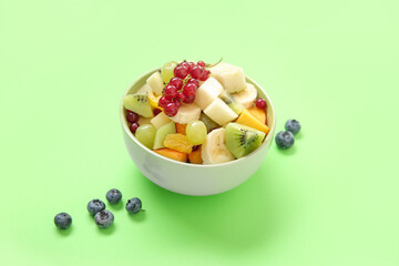 Bowl with fresh fruit salad on green background