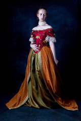 A red-haired Renaissance woman wearing an embroidered silk ensemble against a studio backdrop