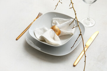 Elegant table setting with golden cutlery, folded napkin and tree branch on white background