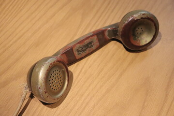 Old phone sleeve in gold color and on wooden background. Vintage telephone handset.