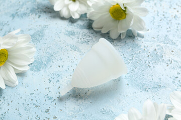 Menstrual cup and beautiful chamomile flowers on color background