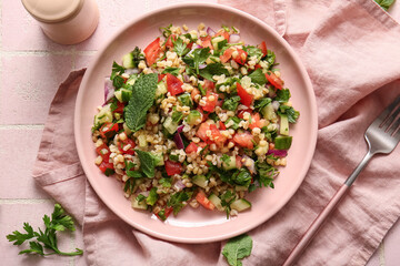 Plate with delicious tabbouleh salad on pink tile background