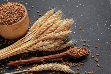 Wooden bowl with grains, wheat ears and spoon on grunge black background