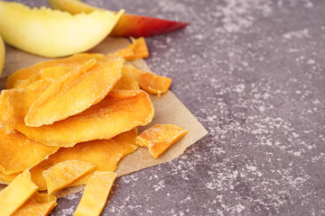 Baking paper with slices of dried mango on dark table