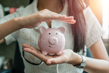 Close-up of a woman holding and protecting a pink piggy bank, representing savings and financial...