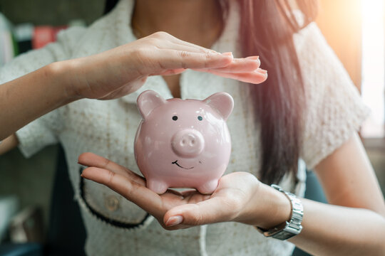 Close-up of a woman holding and protecting a pink piggy bank, representing savings and financial security in a modern environment.