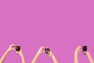 Female hands with glasses of warm mulled wine on pink background